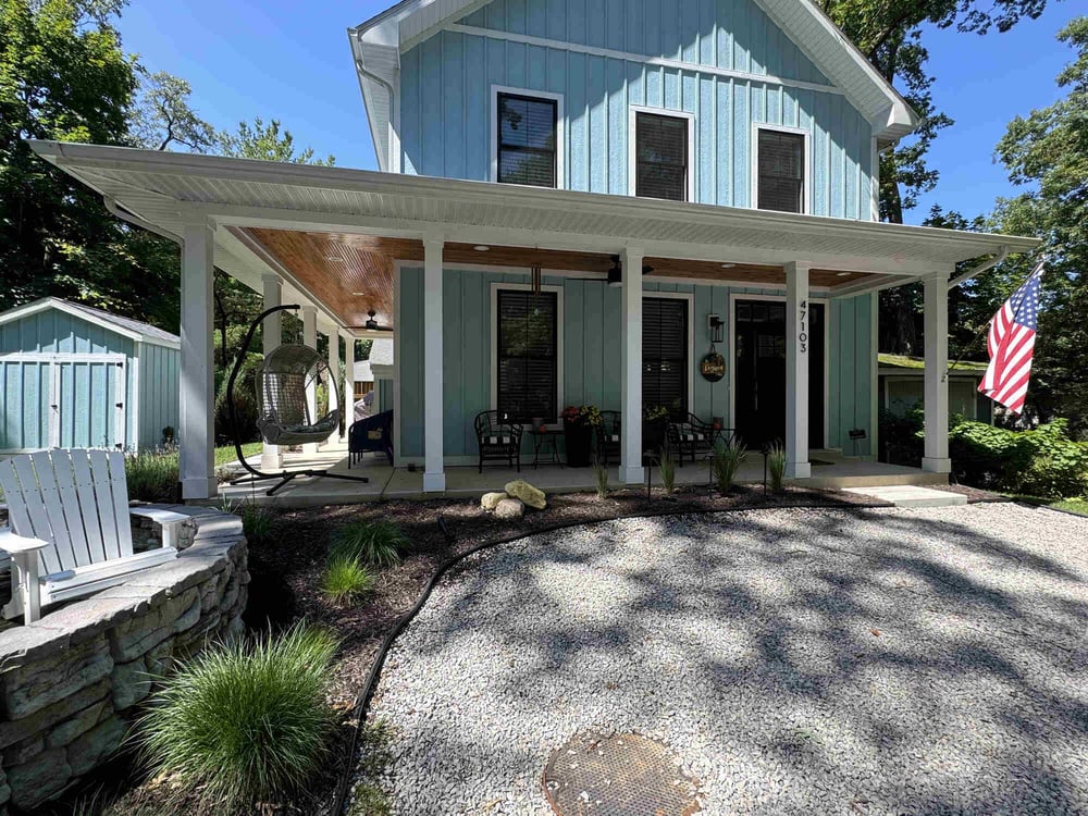 Inviting front elevation of blue custom home with wraparound porch in Grand Beach by Barbour Construction.