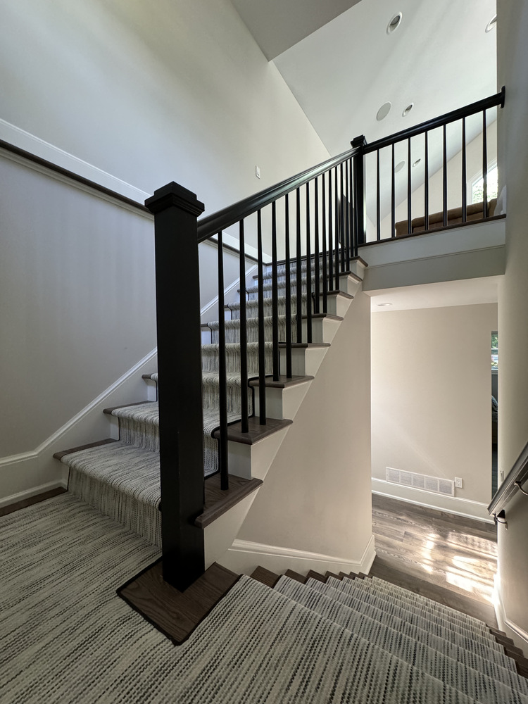 Modern staircase design with dark handrail and soft carpeting by Barbour Construction in South Bend.