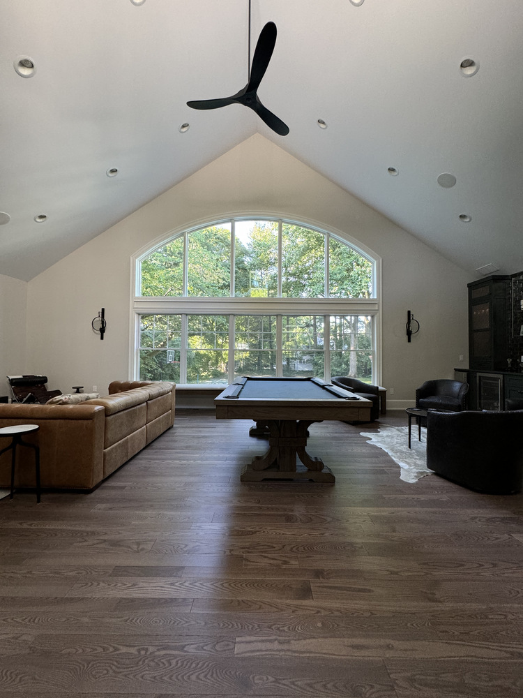 Spacious vaulted ceiling living room with arched window and pool table in a custom South Bend, IN home by Barbour Construction.