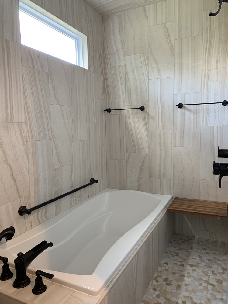 Soaking tub surrounded by large-format tile with matte black fixtures in South Bend custom home by Barbour Construction.
