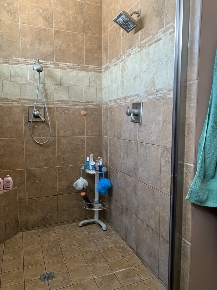 Tile shower with dual showerheads shown in pre-renovation state in South Bend home by Barbour Construction.