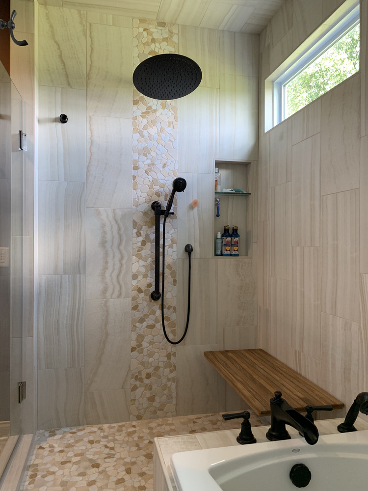 Walk-in shower with rainfall head, stone tile accent, and wood bench in South Bend custom home by Barbour Construction.