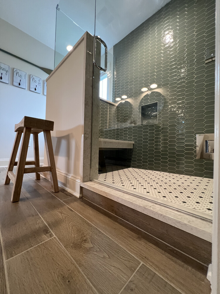 Glass shower enclosure with detailed tile and rustic wood stool in Dowagiac, MI by Barbour Construction.