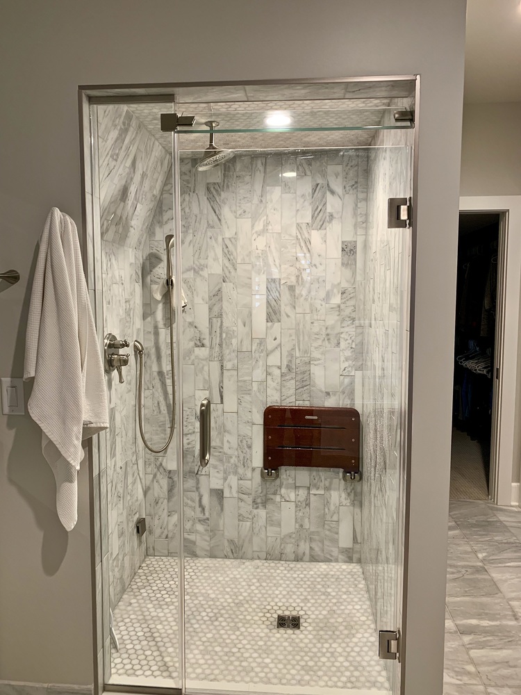 Marble tile walk-in shower with glass door in a Grand Beach custom home by Barbour Construction.