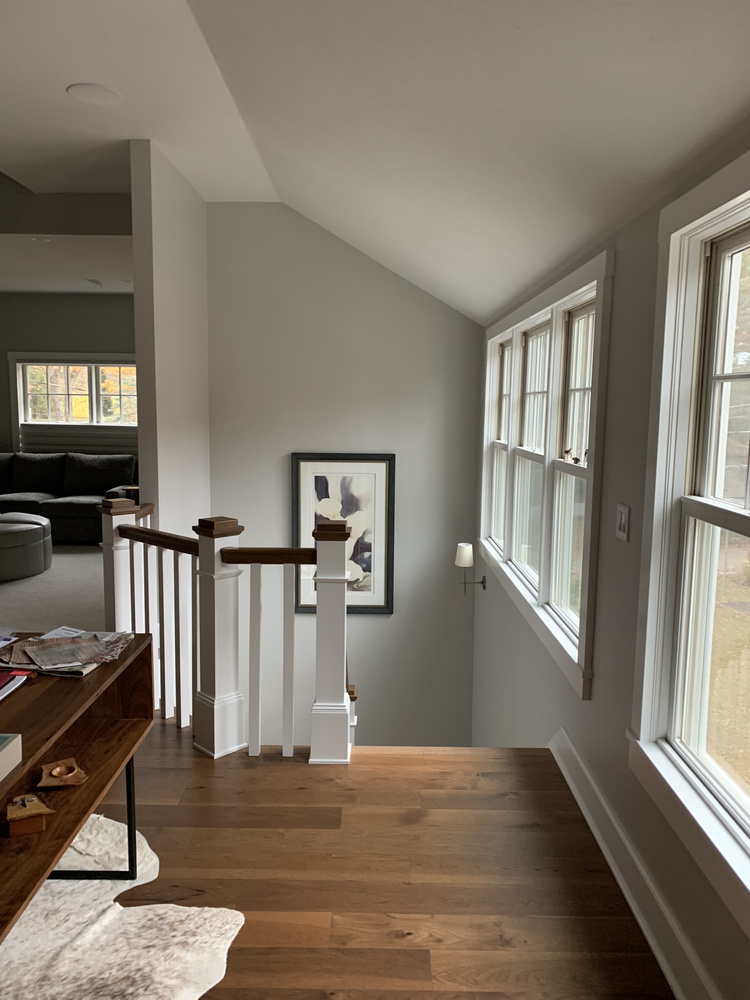Upper stairwell view with large windows and modern railing in a Grand Beach custom home built by Barbour Construction.