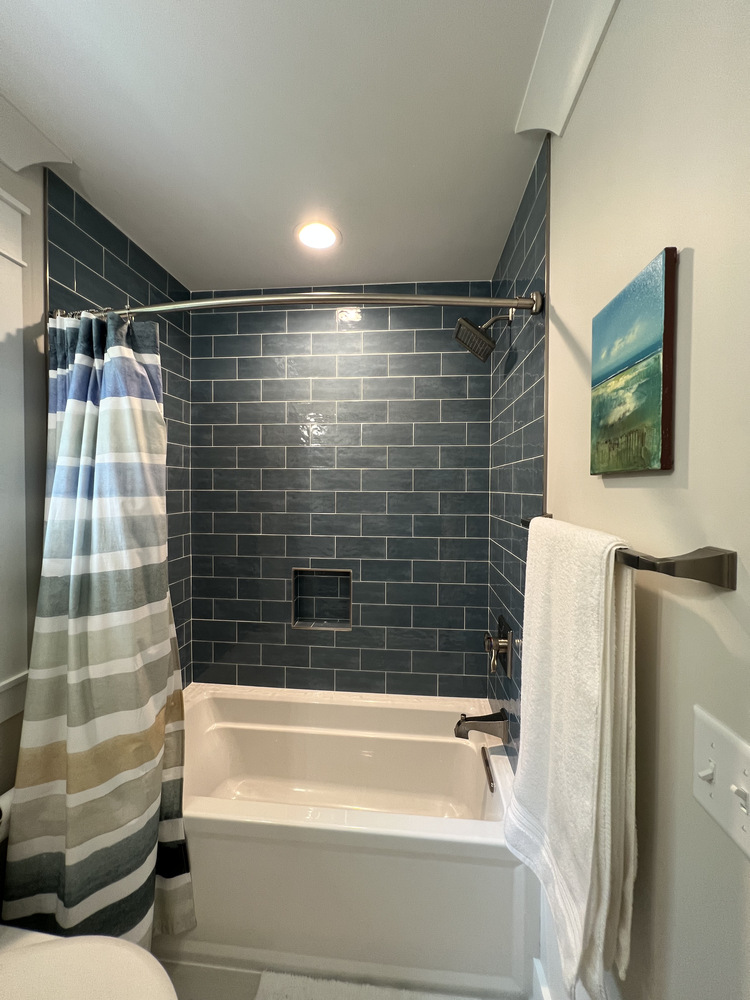 Bathtub with dark blue subway tile and striped shower curtain by Barbour Construction in Grand Beach, MI.