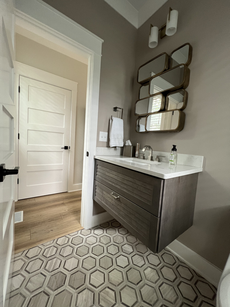 Compact powder room with floating vanity and geometric tile flooring by Barbour Construction in Grand Beach, MI.