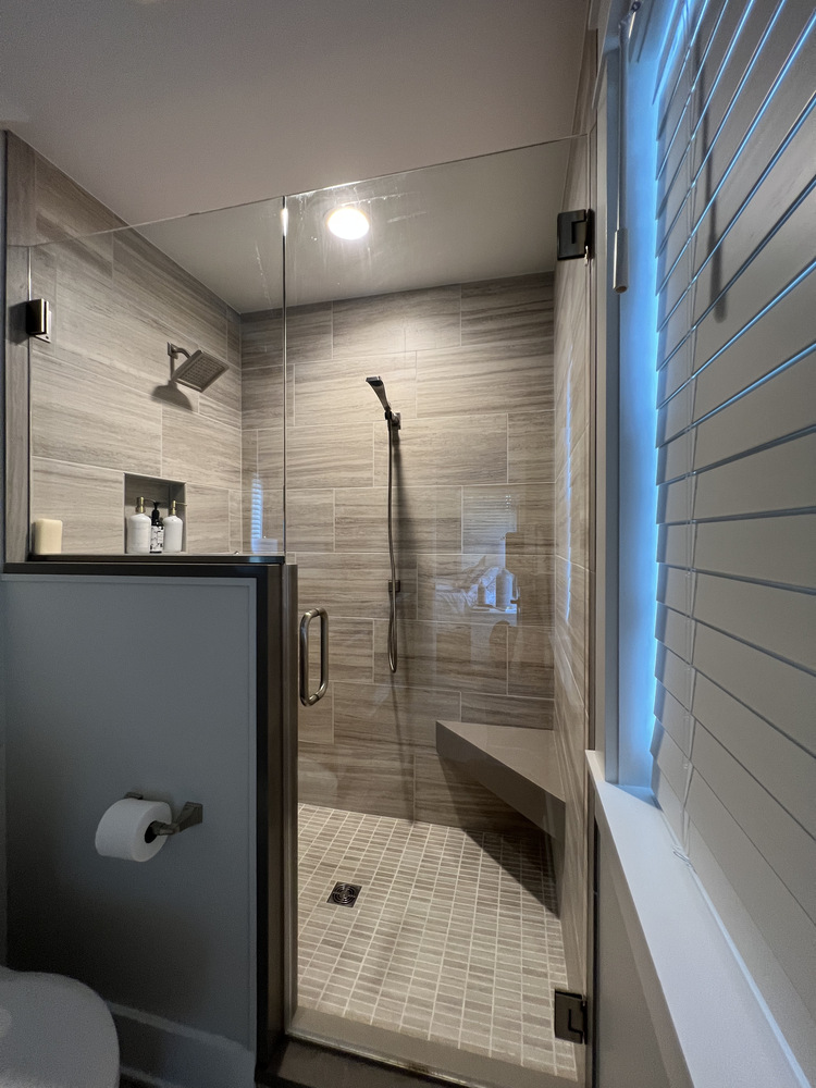 Glass walk-in shower with beige tile in Grand Beach custom home by Barbour Construction.