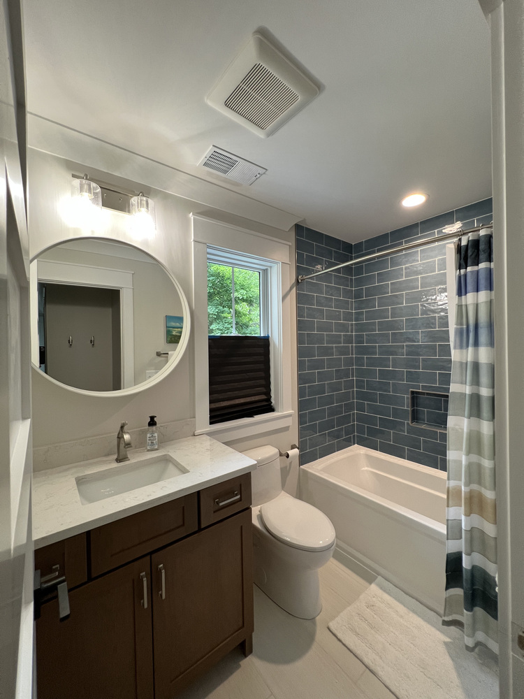 Guest bathroom with blue subway tile and round mirror by Barbour Construction in Grand Beach, MI.