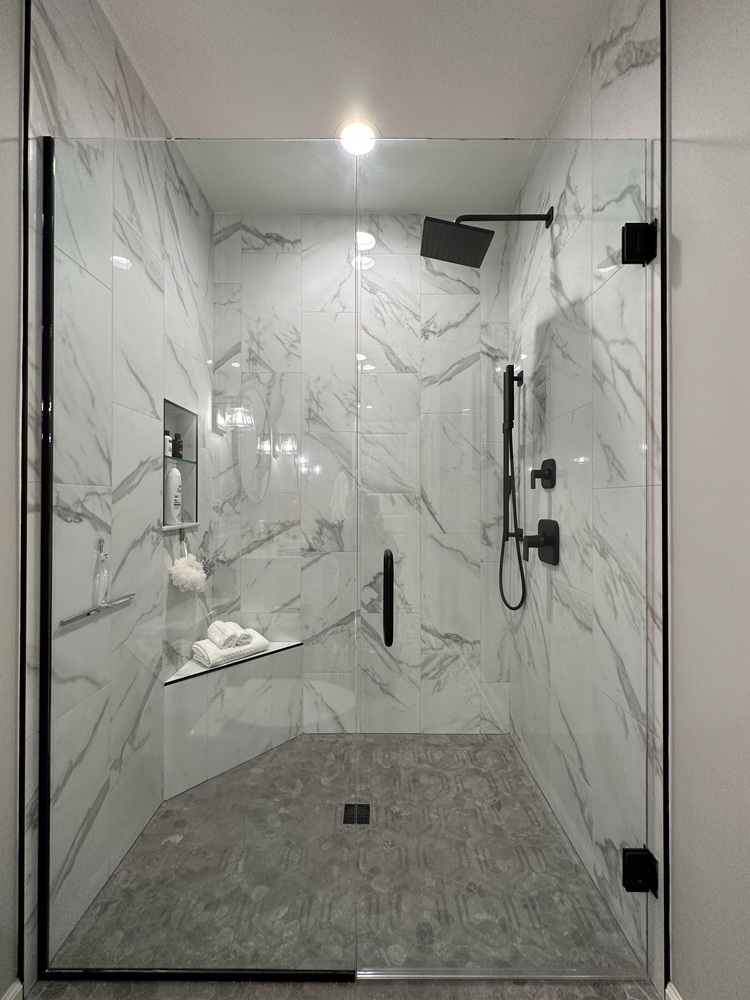 Frameless glass shower with black fixtures and marble tile in New Carlisle home by Barbour Construction.