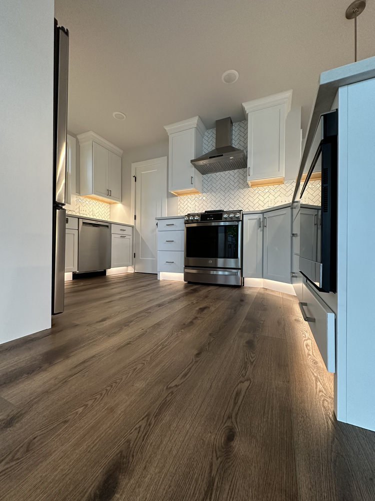 Low-angle view of kitchen showing under-cabinet lighting and hardwood flooring in Sawyer, MI custom home.