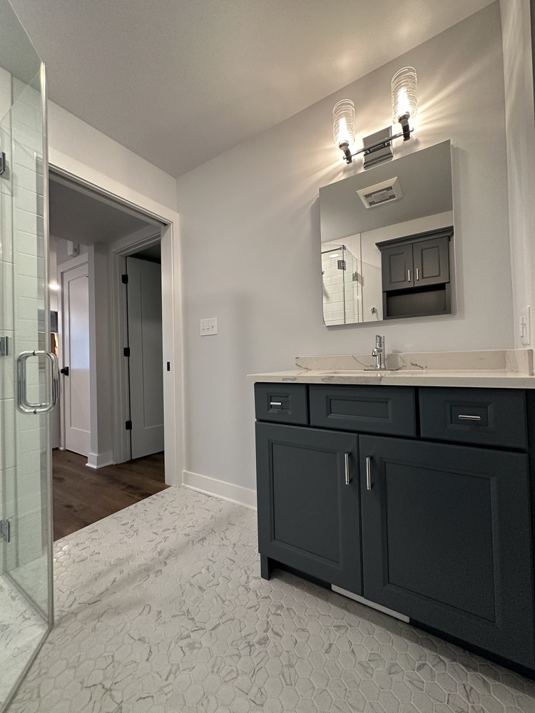 Single-sink vanity with navy cabinetry and modern lighting in Barbour Construction bathroom in Sawyer, MI.