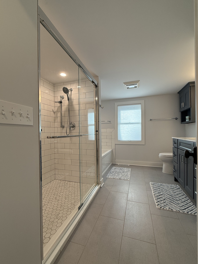 Spacious bathroom with glass walk-in shower and gray tile flooring in custom Sawyer, MI home by Barbour Construction.