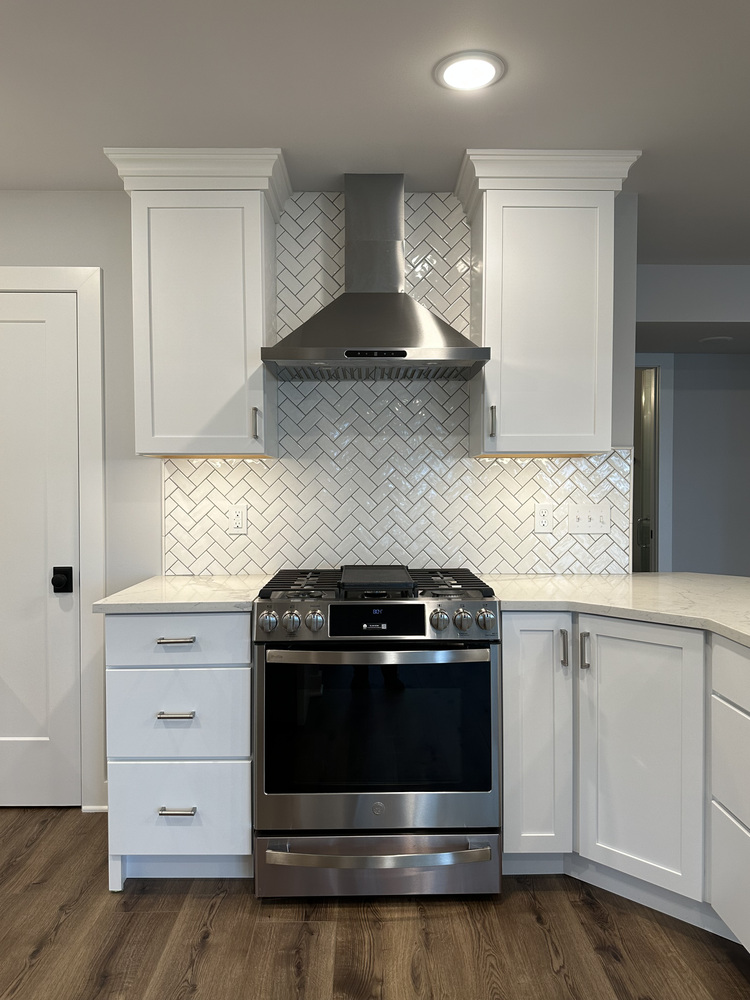 White kitchen with stainless steel range and herringbone backsplash in Sawyer, MI home by Barbour Construction.