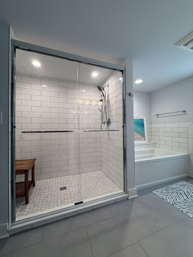 White subway tile shower with wood bench and glass doors in Barbour Construction bathroom in Sawyer, MI.