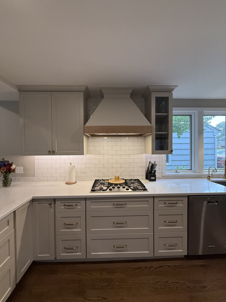 Built-in gas cooktop and custom vent hood in white kitchen by Barbour Construction in South Bend, IN.